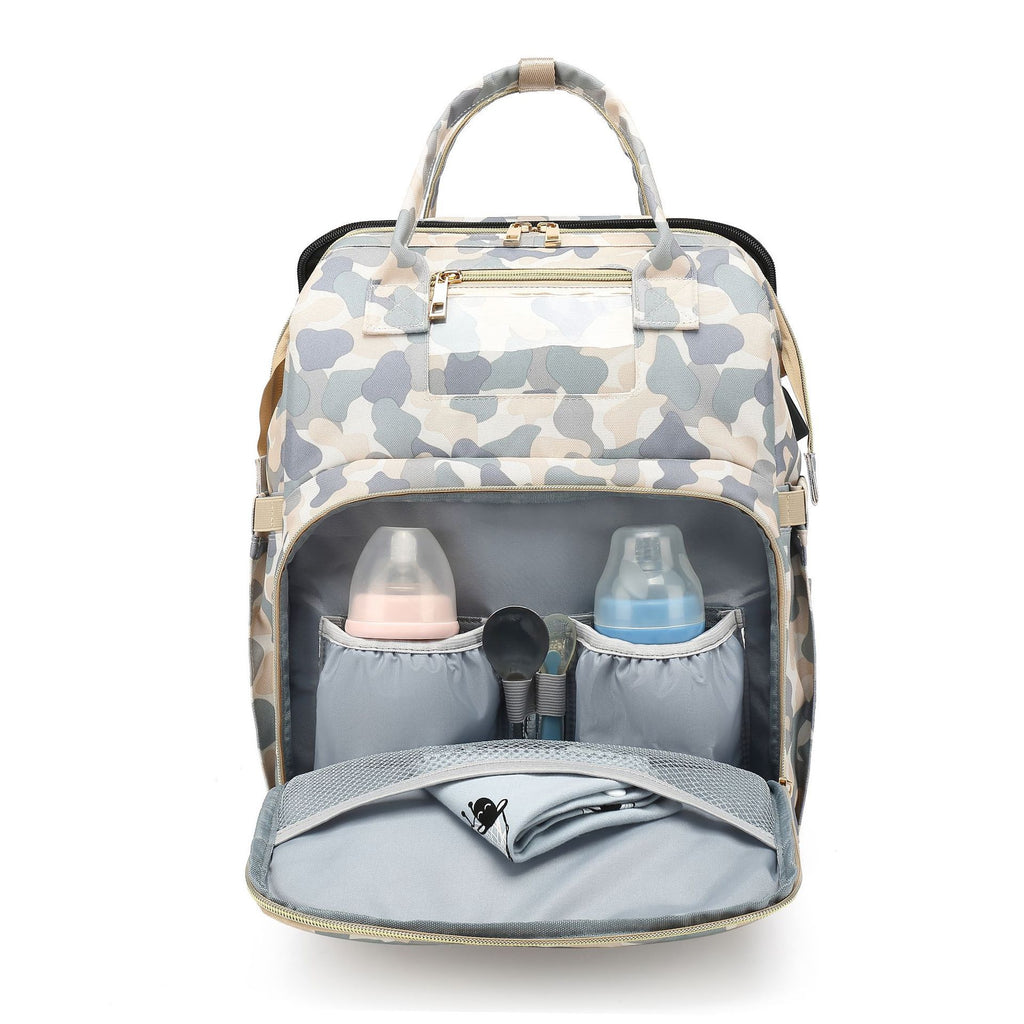 Camouflage diaper backpack with its front compartment open, showing two bottles and storage pockets