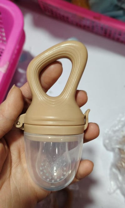 Hand holding a beige baby food feeder with a loop handle and clear protective cap