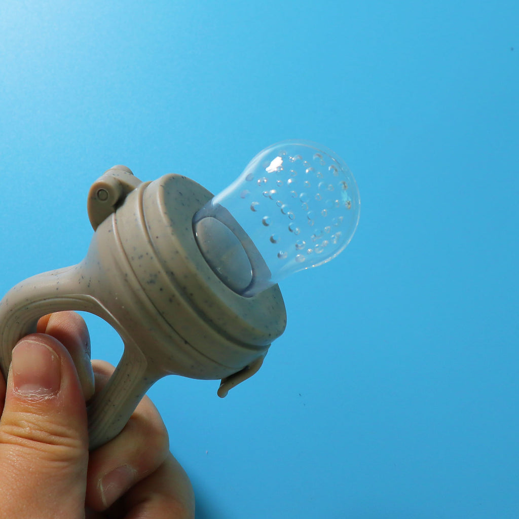Hand holding a gray baby food feeder with its perforated silicone nipple exposed
