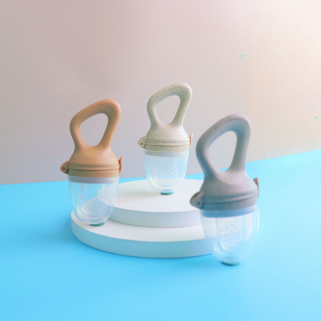 Three baby food feeders with loop handles and clear protective caps on white display stands