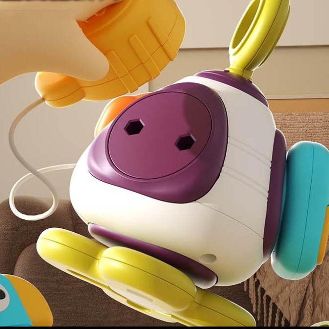Hand lifting a yellow piece attached by a cord to a white and purple baby activity ball